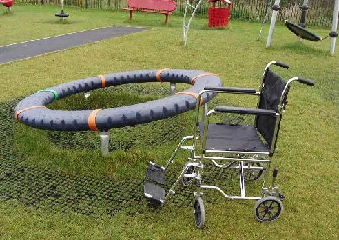 Fauteuil roulant à côté d’un jeu inclusif circulaire sur gazon